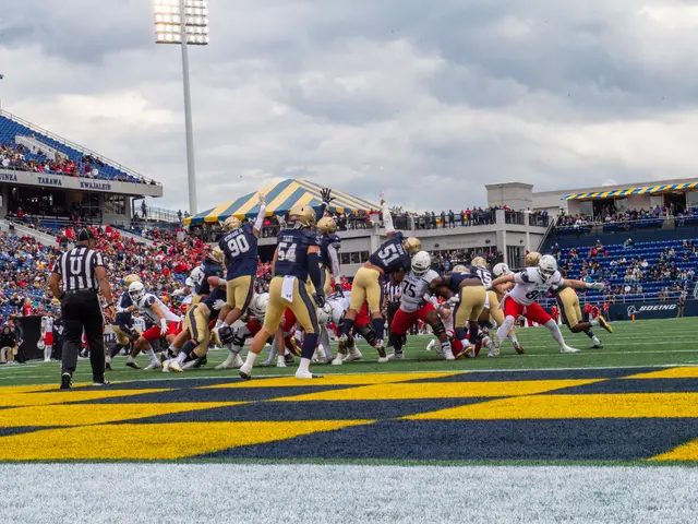 The image shows a football game being played in a stadium, with people wearing sports dress and...
