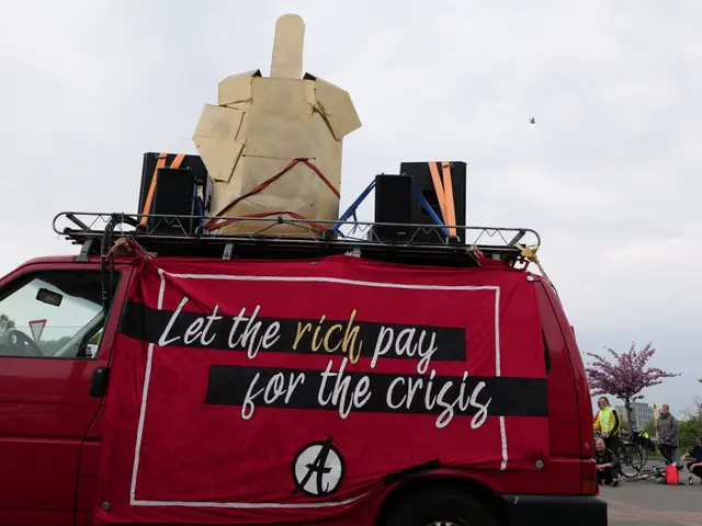 The image shows a red van with a sign on the back of it that reads "Let the Rich Pay for the...