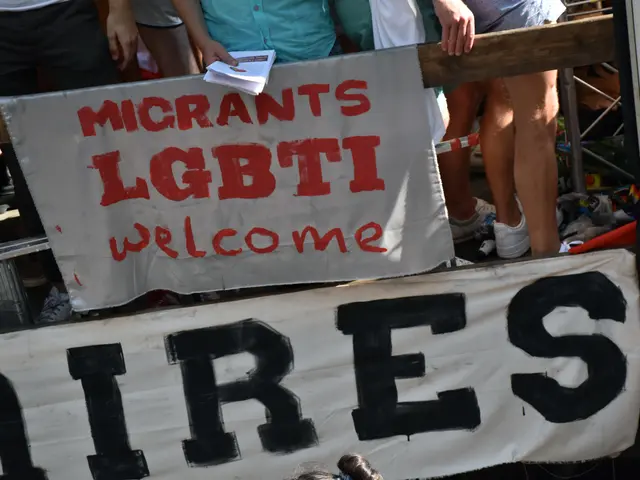 The image shows a group of people standing next to each other, holding a sign that reads "Migrants...