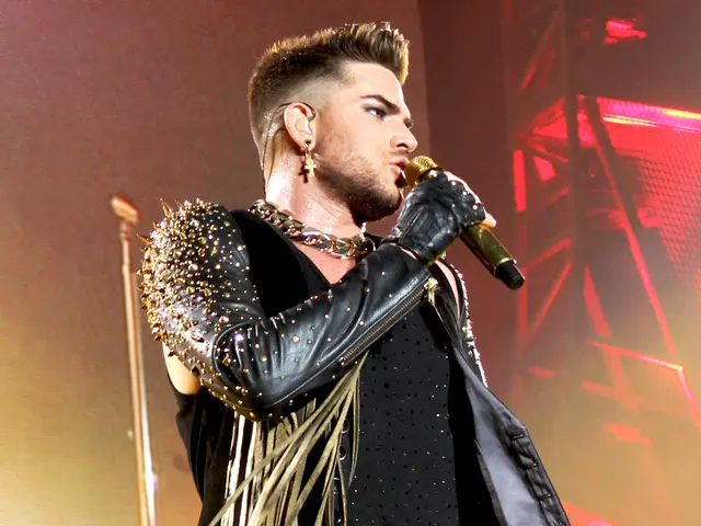The image shows Adam Lambert performing at the O2 Arena in London, wearing a black dress and...