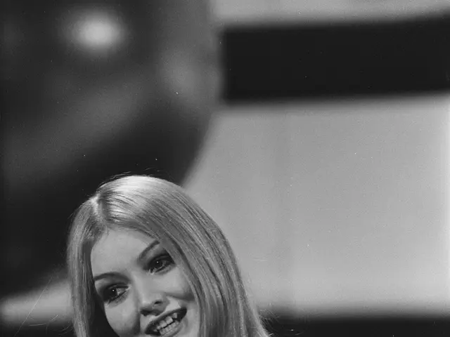 The image shows a woman in a floral dress singing into a microphone with a smile on her face. The...