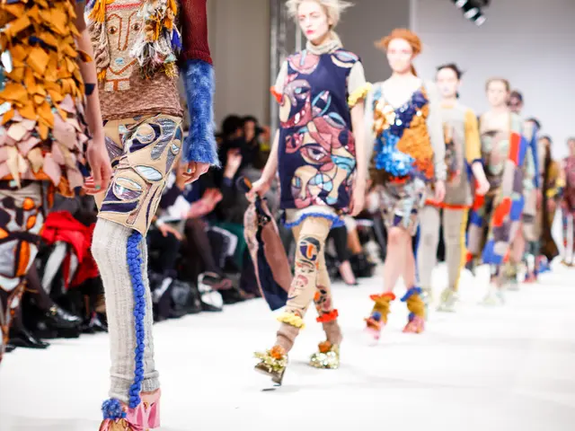 The image shows a group of women walking down a runway at London Fashion Week, with people sitting...