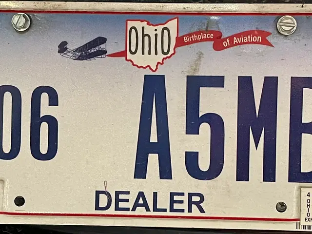The image shows a license plate on the back of a car, with text and numbers written on it.