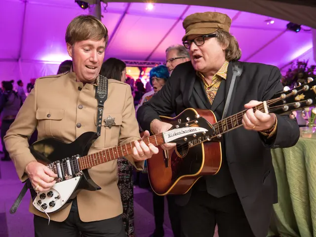 The image shows two men playing guitars in a tent, surrounded by a group of people standing on the...