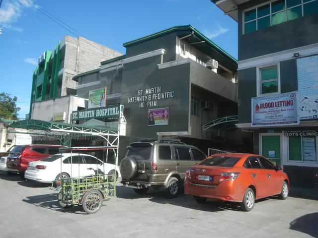 The image shows a hospital with cars parked in front of it, surrounded by buildings with windows,...