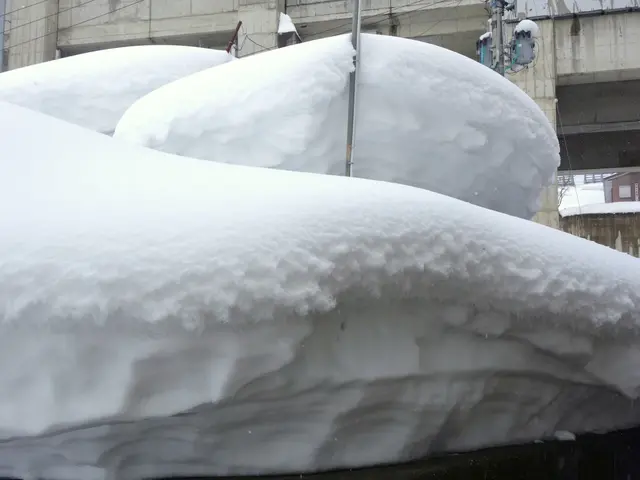 The image shows a large pile of snow on top of a building, with poles, wires, and other objects...