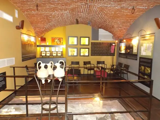 The image shows a room filled with lots of tables and chairs, a railing, vases, boards with text...