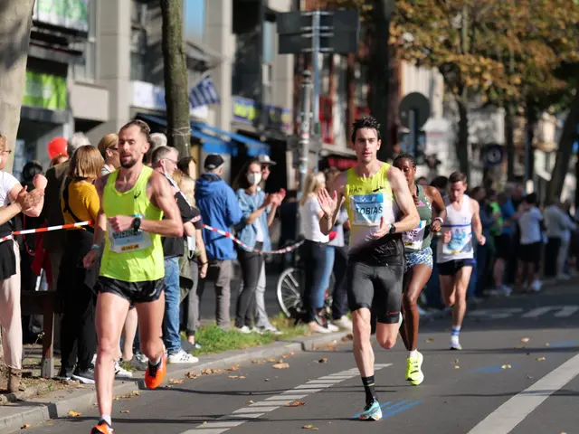 The image shows a group of people running in a marathon on a city street, with a crowd of people...