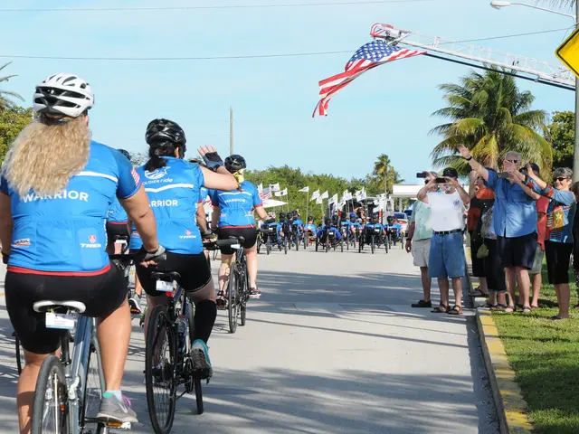 The image shows a group of people wearing helmets and riding bicycles down a street lined with...