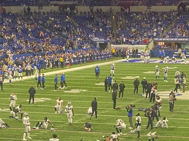 The image shows a football game being played in a stadium, with a group of people standing on the...