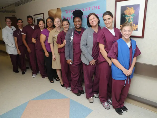 The image shows a group of people in scrubs standing next to each other in a hospital hallway. They...