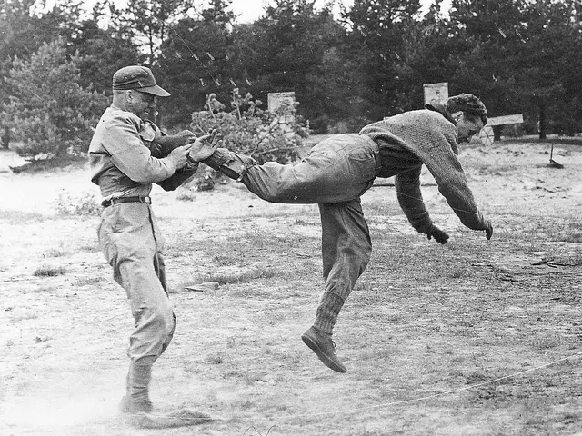 The image shows two men in military uniforms, one wearing a cap and the other wearing boots,...