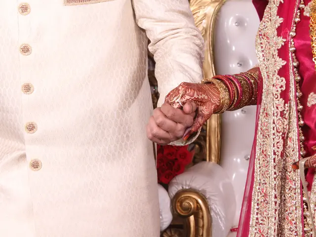 The image shows a bride and groom holding hands during their Hindu wedding ceremony. The bride is...