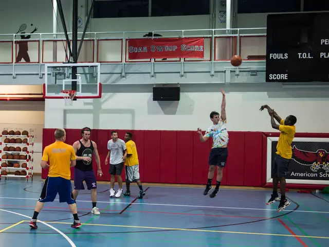 The image shows a group of men playing a game of basketball in a gymnasium. There is a basketball...