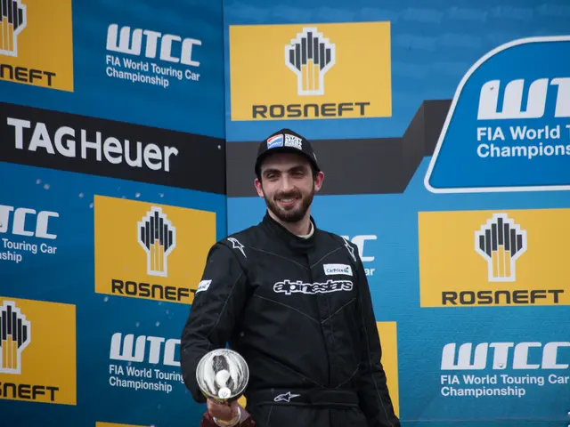 The image shows a man standing on top of a podium, wearing a black dress and a cap, with a big...