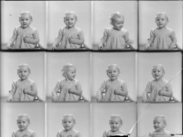 The image shows a black and white photo of a baby with a big smile on their face, surrounded by a...