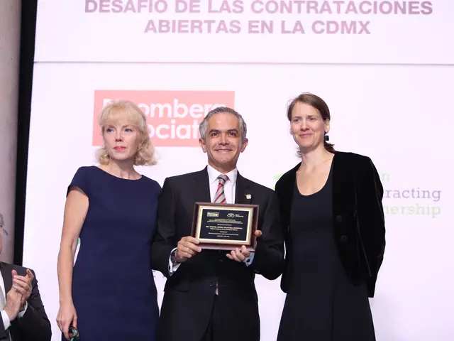 The image shows a group of three people standing next to each other on a stage. The man in the...