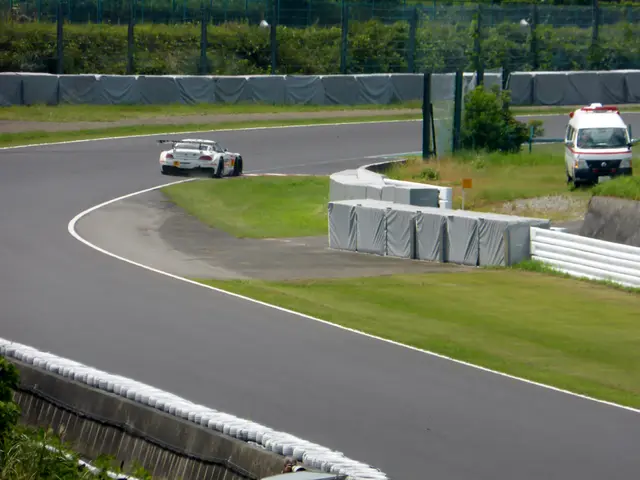 The image shows a race car driving down a race track with a police car in the background. The track...