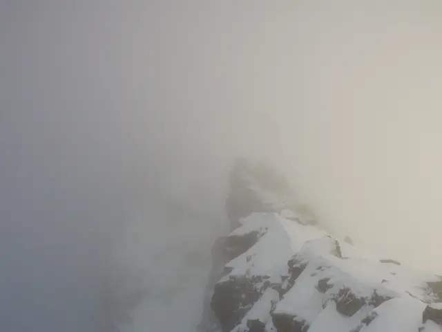 The image shows a snow-covered mountain with a foggy sky in the background. The mountain is...