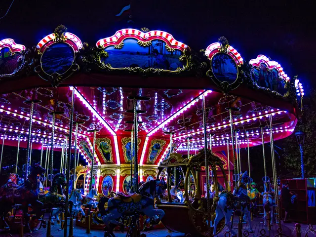 The image shows a carousel at night with people on it, illuminated by colorful lights and...