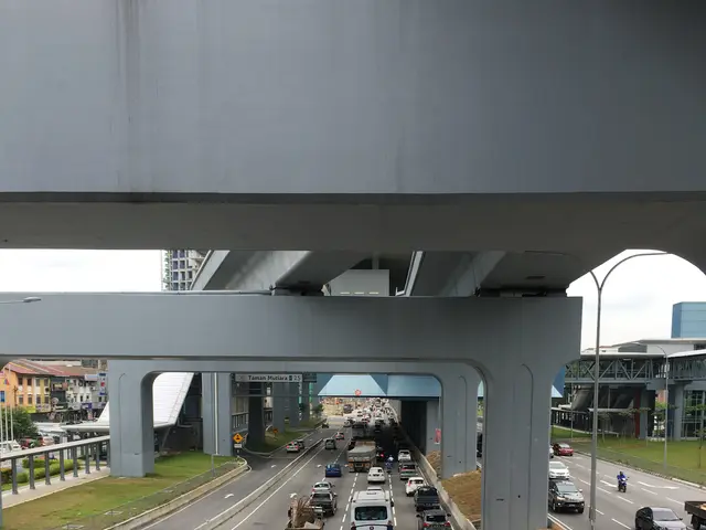 The image shows a highway filled with lots of traffic under a bridge, with vehicles on the road,...