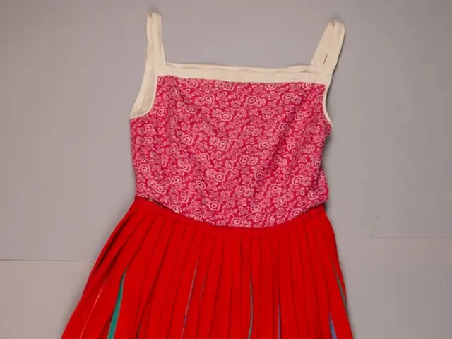 The image shows a red dress with a pink top and green stripes on it, lying on the floor with a...