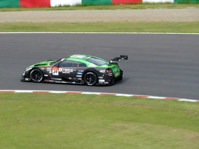 The image shows a sports car driving on a race track with grass on either side of the road and a...