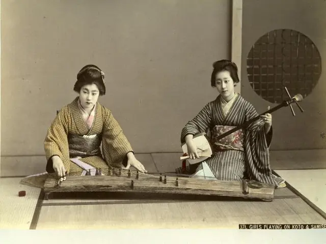 The image shows two women in kimono sitting on the floor playing a koto, a traditional Japanese...