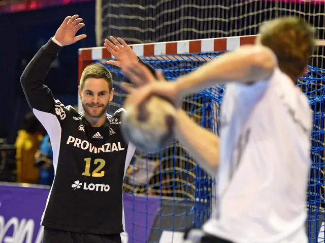The image shows two men playing a game of handball in front of a goal, with a net in the background...
