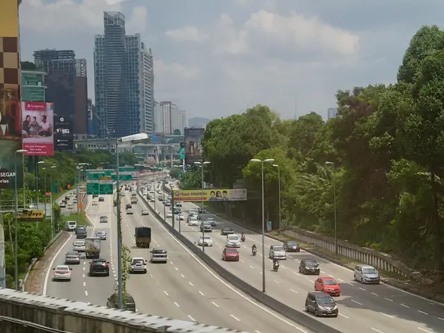 The image shows a highway filled with lots of traffic next to tall buildings, street poles, street...