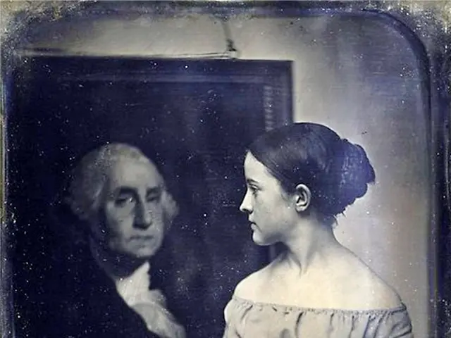 The image shows an old photo of a man and a woman standing side by side. The man is wearing a suit...