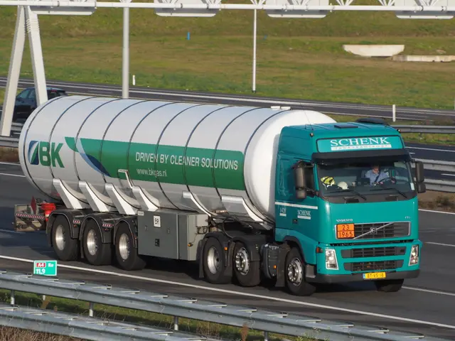 The image shows a large tanker truck driving down a highway, with a person sitting in the driver's...