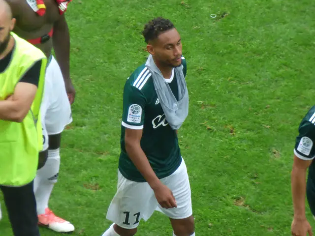 The image shows a group of men standing on top of a soccer field, with one of them wearing...