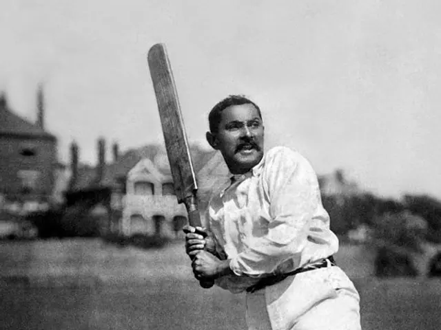 The image shows an old black and white photo of a man playing cricket, standing on the ground and...