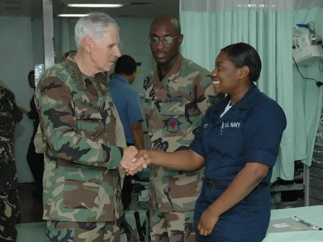 The image shows two men and a woman shaking hands in a hospital room. The woman is wearing a blue...