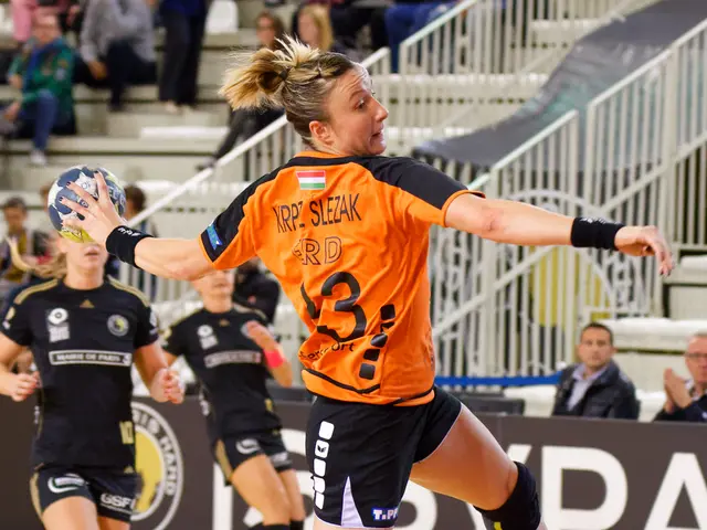 The image shows a woman in an orange shirt and black shorts playing a game of handball, with a ball...