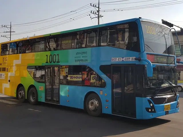 The image shows a blue and yellow double decker bus driving down a street, surrounded by other...