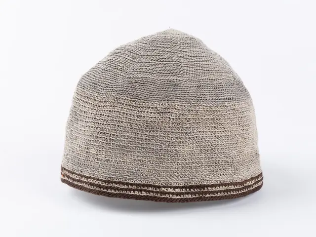 The image shows a beige and brown knitted hat on a white background. The hat is made of wool and...