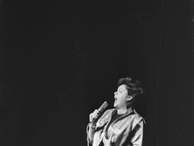 The image shows a woman standing on a stage, illuminated by a spotlight, singing into a microphone....