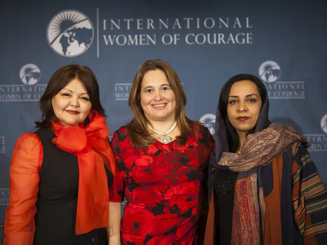 The image shows three women standing next to each other in front of a banner that reads...