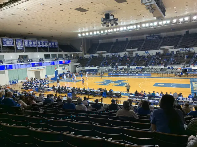 The image shows a large arena filled with lots of people watching a basketball game. There are...