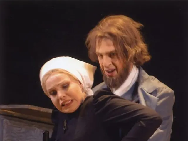 The image shows a man and woman standing next to each other on a stage, with the woman holding a...