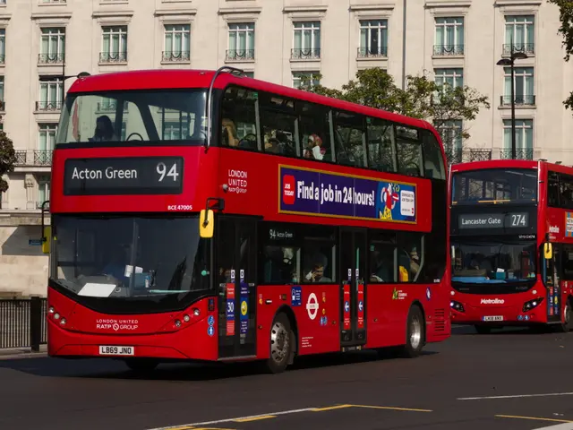 The image shows two red double decker buses driving down a street lined with tall buildings. There...