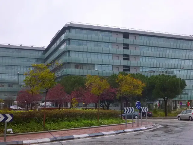 The image shows a large building with many windows on the side of it, surrounded by trees, plants,...
