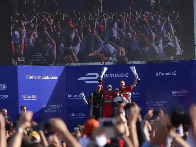 The image shows a group of people standing on top of a race podium, with some of them holding cups...