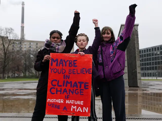The image shows three women standing in front of a building, holding up a sign that reads "Maybe...