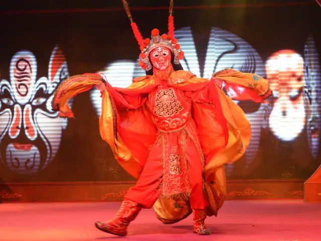 The image shows a man in a red costume performing a Chinese opera on stage, with a screen in the...