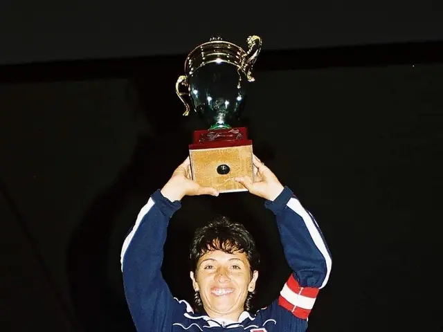 The image shows a woman standing and smiling proudly while holding up a trophy in front of a...