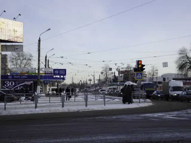 The image shows a city street filled with lots of traffic on a snowy day. There are street lights,...