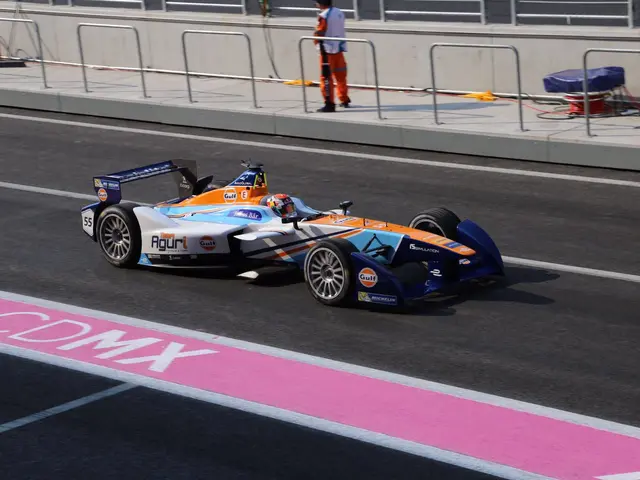 The image shows a man driving a Formula car on a race track, with a person wearing a helmet in the...